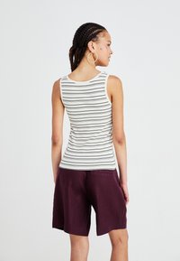 Striped tank top in cream and navy; fitted design. Paired with loose, burgundy shorts. Smooth fabric texture with no visible patterns or accents.