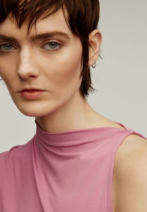 Top rosa sin mangas con cuello alto y diseño drapeado. Textura suave, acentos mínimos y un ajuste relajado que resalta el hombro.