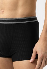 Boxer-briefs noirs avec des rayures verticales, une ceinture élastique grise arborant le nom de la marque, et une coupe ajustée pour plus de confort.