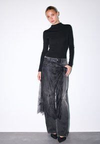 Musta pitkähiha paita; harmaat farkku leveälahkeiset housut pitsikuvioilla; teräväkärkiset mustat korkokengät; minimalistinen muotoilu yksinkertaista taustaa vasten.