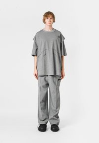 Camiseta gris de gran tamaño con un detalle de costura único, combinada con pantalones anchos grises que presentan acentos laterales y un detalle de cadena. Zapatos negros.