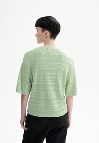 Korte mouwen, mintgroene gebreide top met een horizontale streeptextuur, ronde halslijn en een relaxte fit, gedragen met zwarte broek.