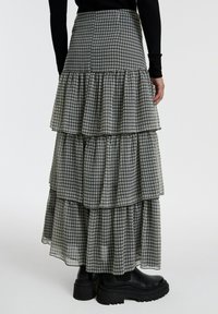 Zwart-wit geruite, gelaagde maxi rok met ruches, voorzien van een hoge taille en een vloeiende snit. Gecombineerd met chunky zwarte enkellaarsjes.