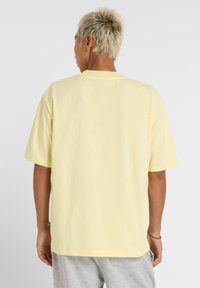 T-shirt jaune à manches courtes en tissu doux. Col rond, coupe décontractée et coutures visibles. La vue arrière présente un design minimal.