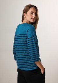 Sininen raidoitettu pitkähihainen paita, jossa on pyöreä kaula-aukko ja rento istuvuus. Tummemmat raidat kulkevat vaakasuoraan kankaan yli.