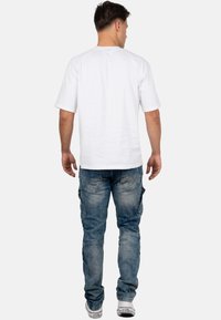 T-shirt bianco a maniche corte abbinato a jeans cargo blu chiaro, sbiaditi, con tasche laterali e vestibilità rilassata. Le sneakers completano l'outfit.