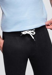 Zwarte joggingsbroek met een elastische tailleband en een witte trekkoord. De broek heeft zijzakken en een gladde textuur. Gepaard met een lichtblauw shirt.