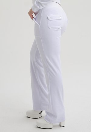 Pantaloni bianchi realizzati in un tessuto morbido con una vestibilità rilassata. Presentano due tasche posteriori con bottoni a pressione e una texture liscia. Abbinati a scarpe con la zeppa bianche e generose.