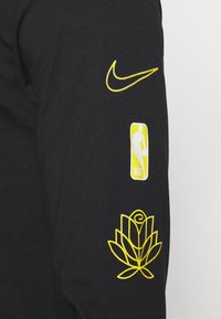 Czarna koszulka z długim rękawem z żółtym haftowanym logo Nike, logo NBA oraz grafiką róży na rękawie. Wykonana z bawełny, w stylu casual.
