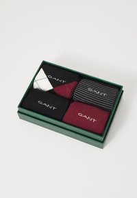 Vier Paar Socken in einer grünen Box: einfarbig schwarz, gestreift schwarz und grau, kastanienbraun und ein Argyle-Muster in Weiß, Schwarz und Rot.