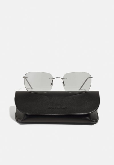 Lunettes de soleil en métal avec des verres gris reposant sur un étui en cuir noir. L'étui présente une texture lisse et un logo en relief.