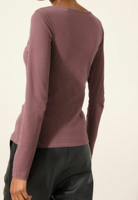 Pitkiä hihoja, ribattua mauve-väriä olevaa puseroa, jossa on pyöreä kaula-aukko. Kankaassa on pehmeä tunne ja se on muotoiltu istuvaksi. Yhdistetty mustiin housuihin.