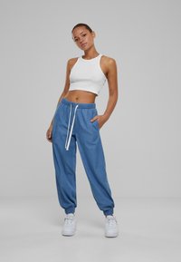 Pantalones de chándal de ajuste suelto en azul claro, con cintura elástica y cordón blanco. Combinados con un top corto blanco. Textura de tela suave.