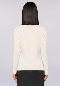 Suéter de manga larga color crema con cuello redondo y puños de canalé, hecho de una tela suave con una textura lisa. Diseño simple y clásico.
