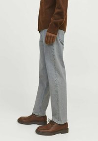 Cárdigan de punto marrón, jeans rectos de tiro medio en azul claro y zapatos de cuero marrón oscuro. Presenta puños acanalados y detalles texturizados en los zapatos.