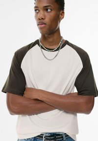 Cream and dark green raglan t-shirt, short sleeves, cotton material. Model wears layered necklaces. Simple design with a relaxed fit.