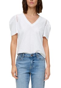 Witte katoenen T-shirt met een V-hals en pofmouwen, met kantdetails op de schouders. Gecombineerd met lichtblauwe denim jeans.