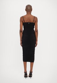 Abito bodycon nero con spalline sottili regolabili, dettagli di arriccio e lunghezza fino al polpaccio. Chiusura con zip sul retro visibile.