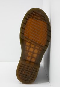 Suela de un zapato con material de goma marrón, superficie texturizada con patrones de tracción y detalles de marca en relieve.