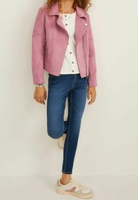 Jasnoróżowa, sztuczna skórzana kurtka motocyklowa z detalami zamka, zestawiona z białą, prążkowaną bluzką i niebieskimi, obcisłymi dżinsami. Sneakersy mają różowe akcenty.