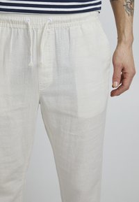 Pantalones de lino de color claro con cinturilla elástica y cordón. Textura suave con un ajuste holgado, que cuenta con bolsillos frontales.