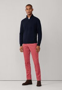 Marine blauwe ritstrui, rode broek, bruine enkellaarsjes. Slim fit, ribbelboorden en -zoom. Soepele textuur, effen kleuren, minimale details.
