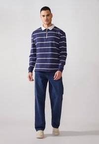 Navy striped long-sleeve polo with a white collar, half-zip front, and a small logo. Paired with loose-fitting blue jeans and light sneakers.