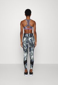 Sportovní podprsenka v purpurové barvě s designem na závodní záda; legíny s vysokým pasem s černým a abstraktně šedým vzorem; doplněné černými akcenty.