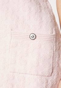 Tissu rose clair texturé avec une poche avant ornée d'un bouton rond argenté décoratif et une couture horizontale au-dessus.