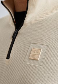 Beżowy sweter na zamek z prążkowanym wysokim kołnierzem, fakturowanym splotem, czarnym detalem zamka oraz wyraźną kremową metką z napisem "PME Legend."