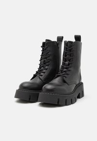 Bottes noires en cuir à chevalières avec des semelles plates épaisses, finition texturée, lacets à l'avant, fermeture éclair sur le côté et tirettes.