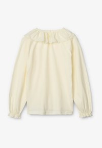 Maglietta a maniche lunghe in morbido tessuto giallo chiaro. Presenta un colletto arricciato con bordi scallop e chiusura con bottone sul retro. Polsini elasticizzati.