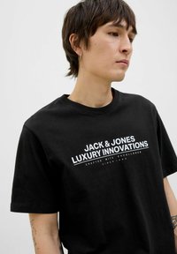 Svart bomulls t-shirt med korta ärmar och rund halsringning. Har vit text: "JACK & JONES LUXURY INNOVATIONS" på framsidan.