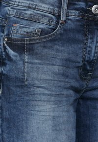 Jeans de denim en azul oscuro con un efecto desgastado, que cuentan con dos bolsillos frontales y costuras en naranja contrastante a lo largo de las costuras y los bolsillos.