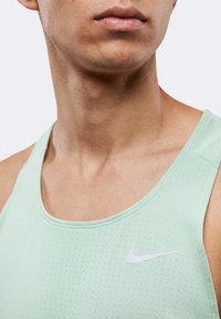 Gros plan d'une personne portant un débardeur Nike vert clair perforé, se concentrant sur le cou, le bas du visage et le haut de la poitrine.