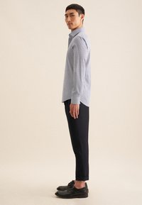 Lichtblauw langarm shirt met witte stippen, gecombineerd met marineblauwe cropped broek en zwarte schoenen, weergegeven in een zijprofiel.