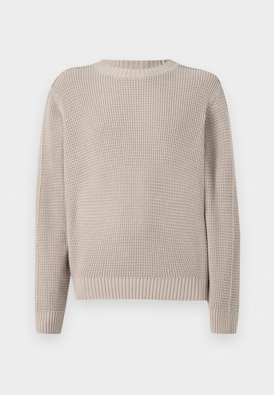 Pull beige à manches longues en maille avec une texture gaufrée, col rond, poignets et bas côtelés sur fond uni.