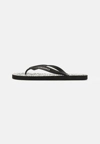 Svart flip-flop med teksturert hvit fotseng, med et repetitivt geometrisk mønster og tynne svarte stropper. Merkevaren er synlig på stroppen.