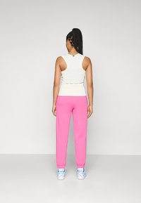 White sleeveless top with a fitted design, paired with bright pink joggers, featuring ribbed cuffs and blue accent shoes.
