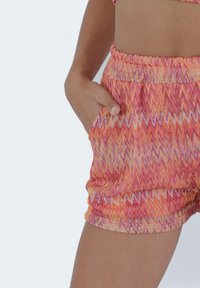Pantaloni corti colorati con un motivo a zigzag in arancione, rosa e giallo. Vita elastica e tasca laterale visibile. Tessuto morbido.