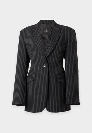 Mulher vestindo um blazer preto risca de giz e calças largas combinando, com uma camisa branca e sapatos slingback pretos de salto.
