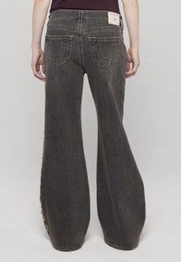 Jeans de pierna ancha en denim lavado oscuro; incluyen bolsillos traseros bordados y cintura alta con detalles de botones a lo largo de las costuras laterales.