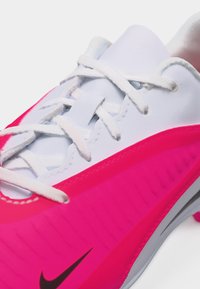Λευκό και ροζ αθλητικό παπούτσι Nike με λευκά κορδόνια και μαύρο λογότυπο Nike, κοντινή λήψη στην επάνω και πλάγια λεπτομέρεια.