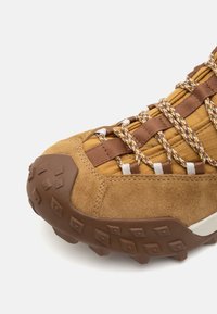 Scarpa da hiking in suede marrone e tessuto con suola in gomma testurizzata dotata di scanalature profonde, e lacci intrecciati per una vestibilità sicura.