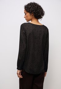Schwarze Bluse mit langen Ärmeln und Leopardenmuster. Durchsichtiger Stoff, lockere Passform und runder Halsausschnitt, mit leicht geschwungenem Saum.