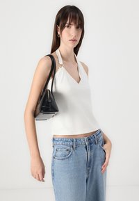 White sleeveless top with a v-neck and silver hardware, paired with light blue loose denim jeans and a small black handbag.