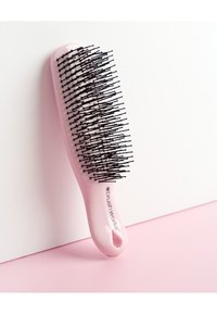 Pink oval hairbrush with black flexible bristles resting against a white surface on a pink background.