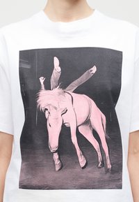 Personne effectuant un équilibre sur les mains sur un cheval, représentée en imprimé rose et noir sur un T-shirt blanc.