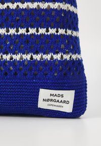 Plava heklana torba s bijelim prugastim uzorkom, koja sadrži oznaku s natpisom "MADS NØRGAARD COPENHAGEN" na pravokutnoj naljepnici.