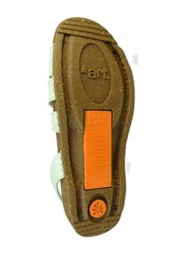 Suela de zapato verde y marrón con superficie texturizada. Incluye una etiqueta naranja que detalla materiales y características ecológicos. Toque circular en el talón.